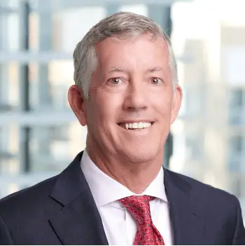 Businessman in navy suit with red tie smiling in an office setting.
