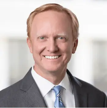 Smiling man in a gray suit and light blue tie, professional headshot.
