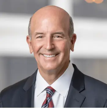 Smiling bald professional man in a dark suit and red striped tie.