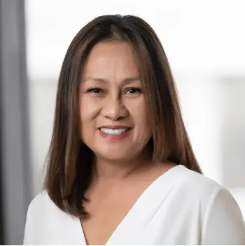 Smiling woman with shoulder-length dark hair in a white blouse against a light blurred background.