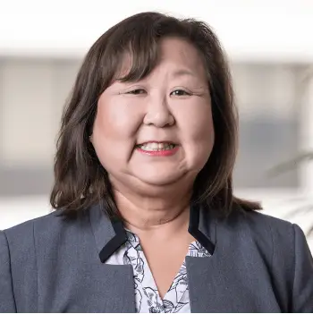 Smiling professional woman with shoulder-length dark hair wearing a navy blazer and patterned blouse.