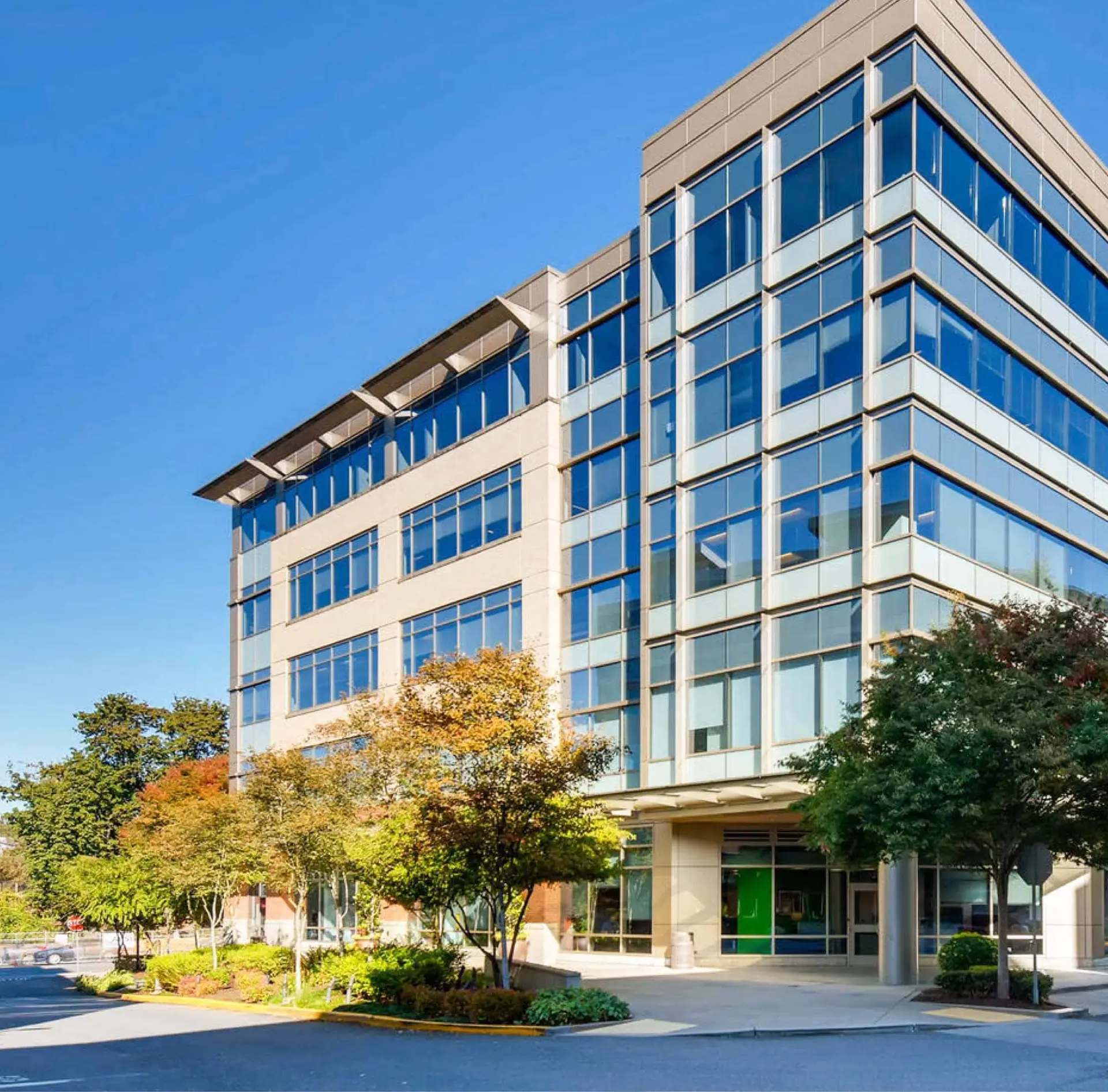 Modern office building stands on a landscaped street corner, under a clear blue sky.