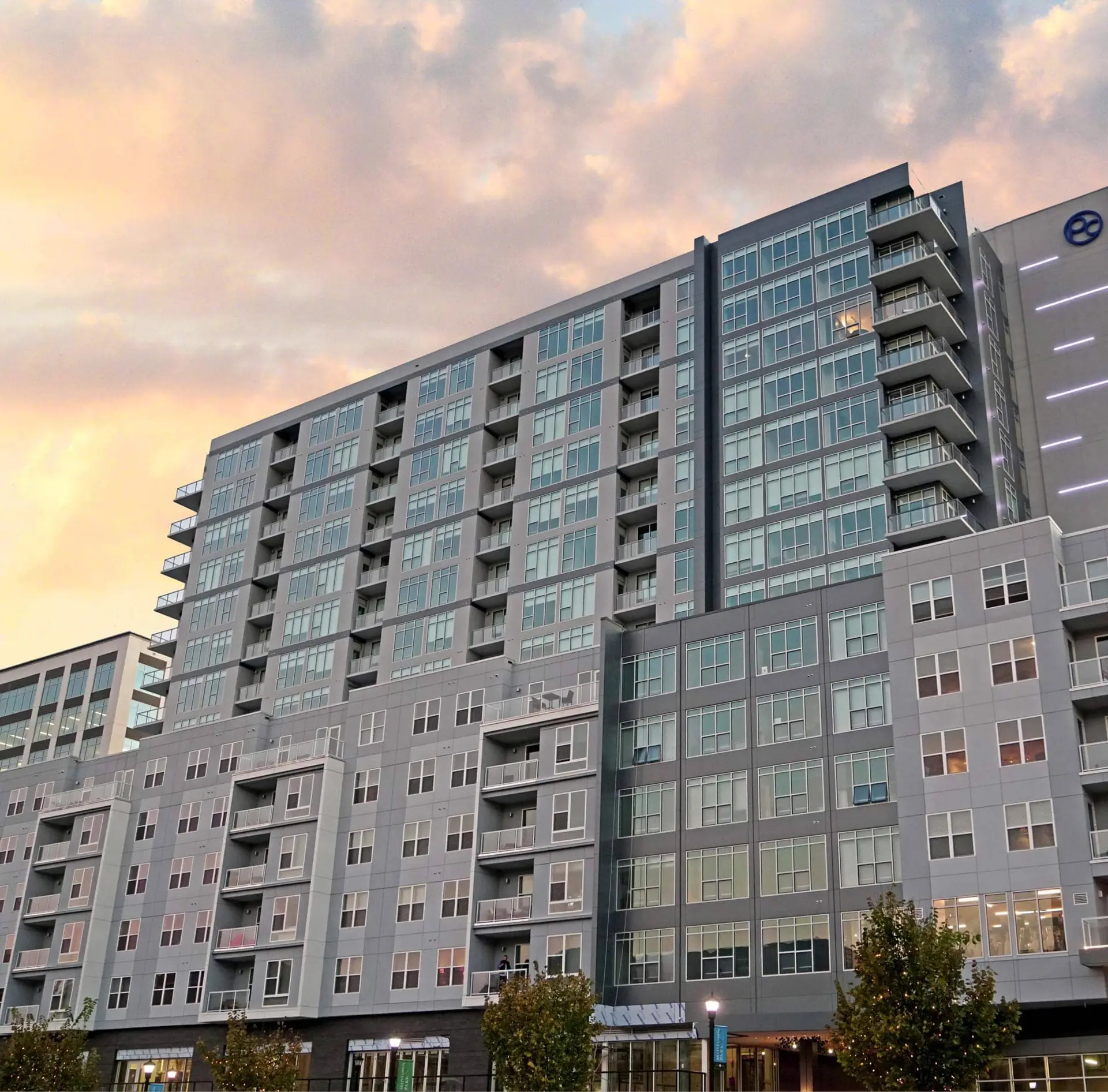 Modern apartment building stands at dusk, under a soft pink sky.
