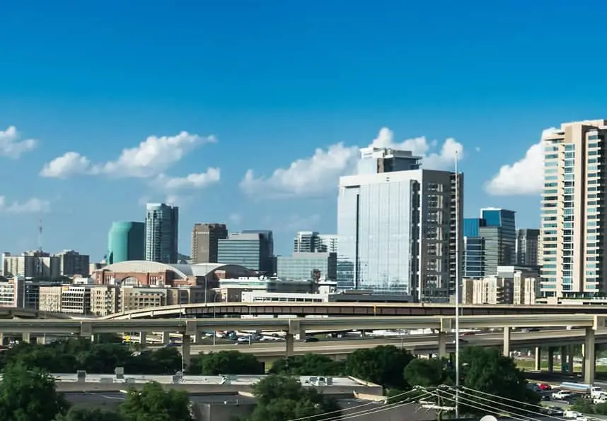 City skyline with skyscrapers, intersected by elevated highways, under a partly cloudy blue sky.