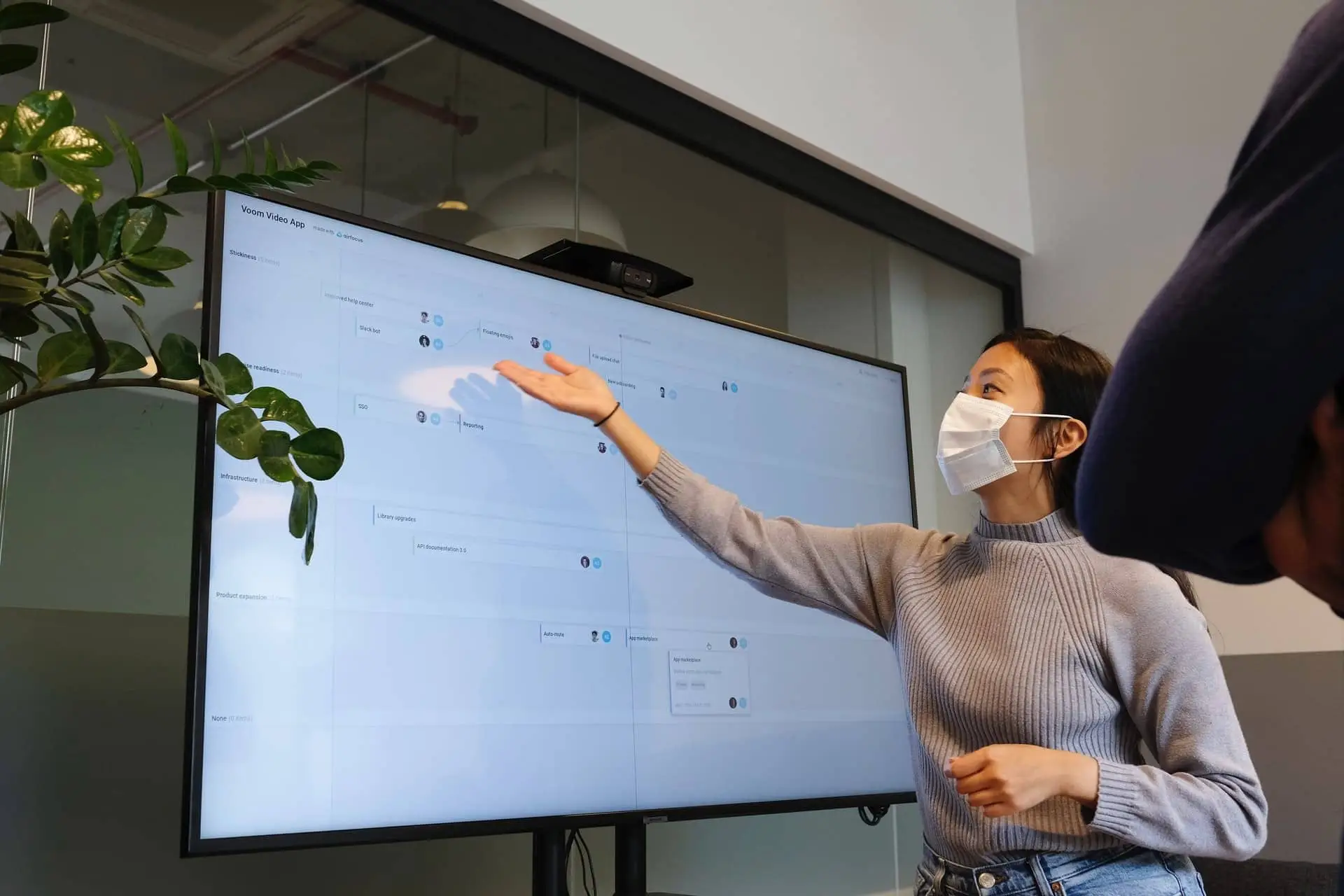 Woman presents project plan on large screen; office setting.