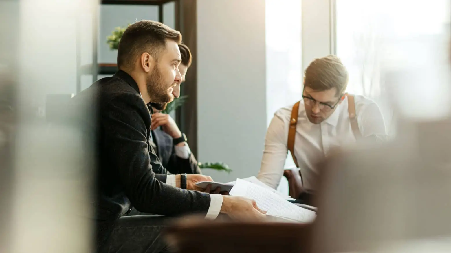 Three professionals discuss documents in a modern, sunlit office.