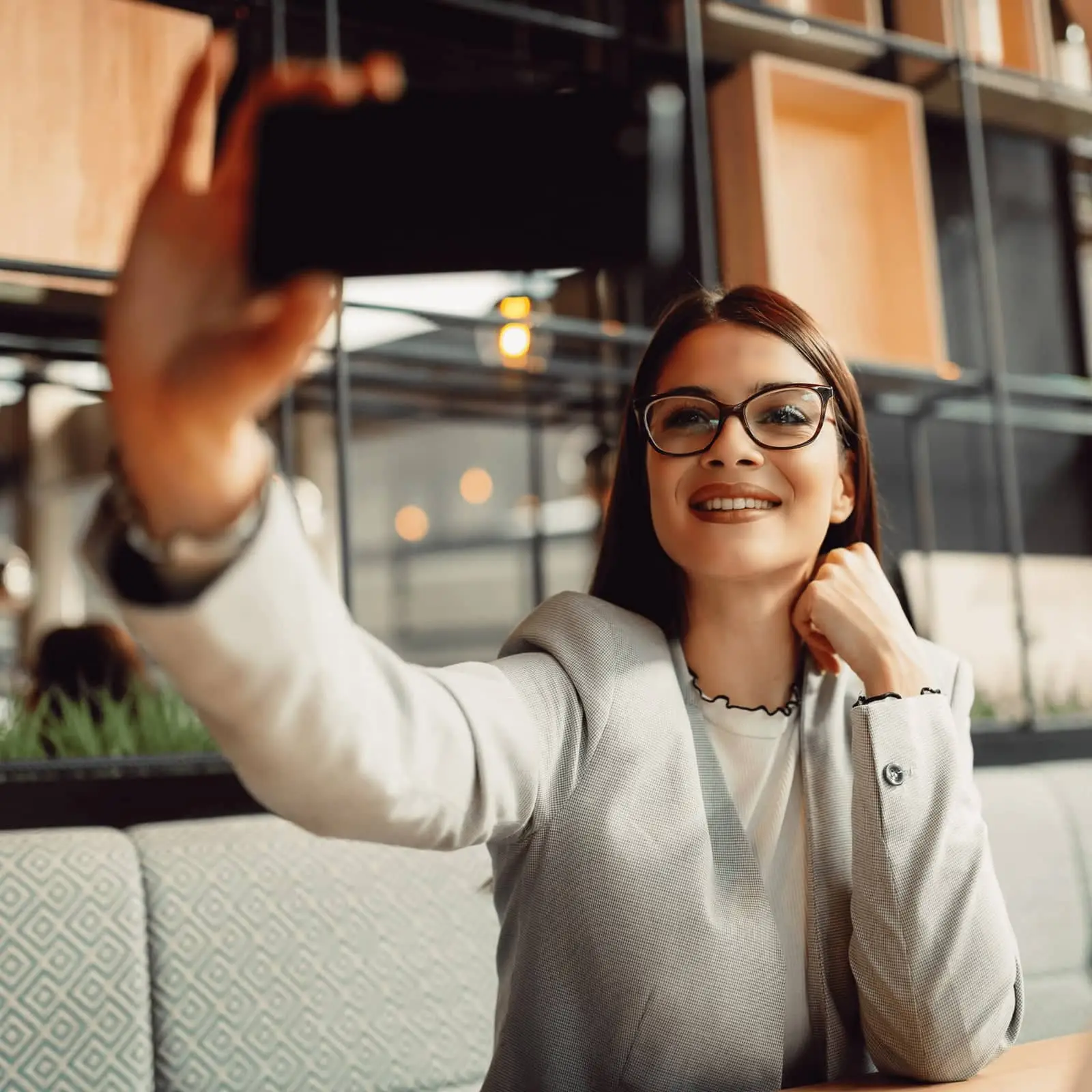 Smiling woman with glasses taking a selfie in a modern cafe.