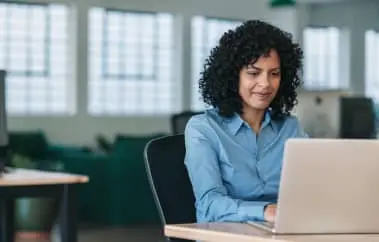 Woman uses laptop, sitting at desk in modern office.