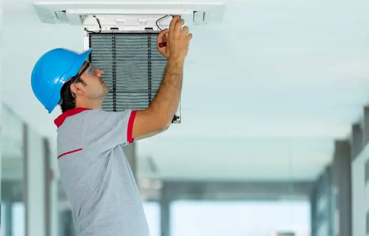 Technician repairs ceiling AC unit filter, inside building.