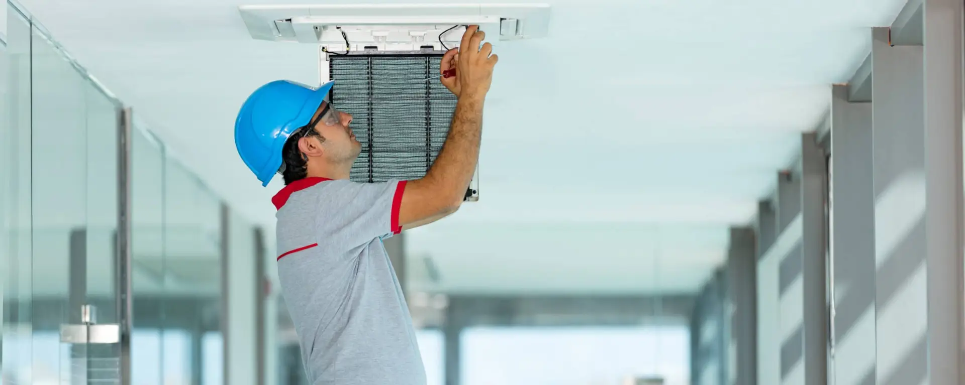 Technician repairs ceiling AC unit in modern hallway.