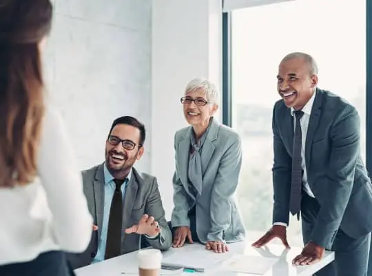 Group of professionals in a modern office, smiling and discussing around a conference table.