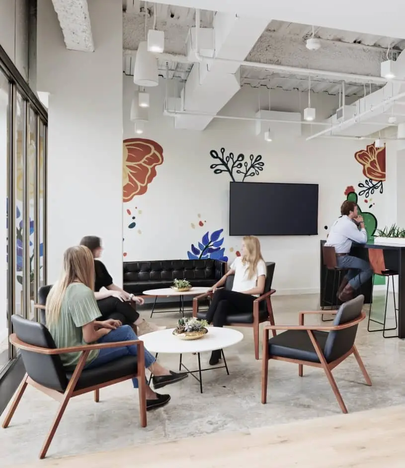 People converse in mid-century modern armchairs around a small table, in a brightly lit office featuring a floral wall mural.