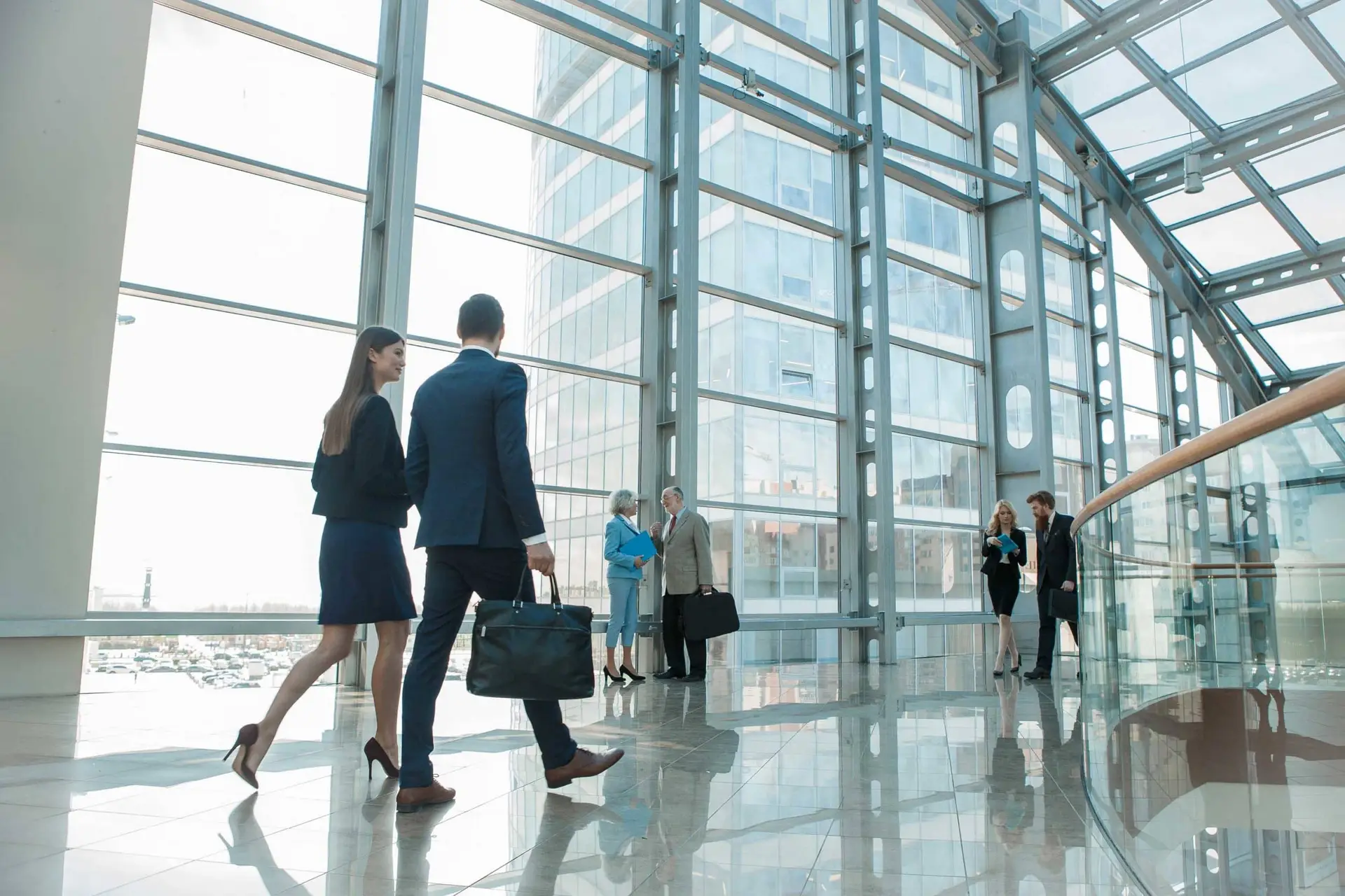 Business professionals in formal attire walk through a bright glass atrium in a modern office building.