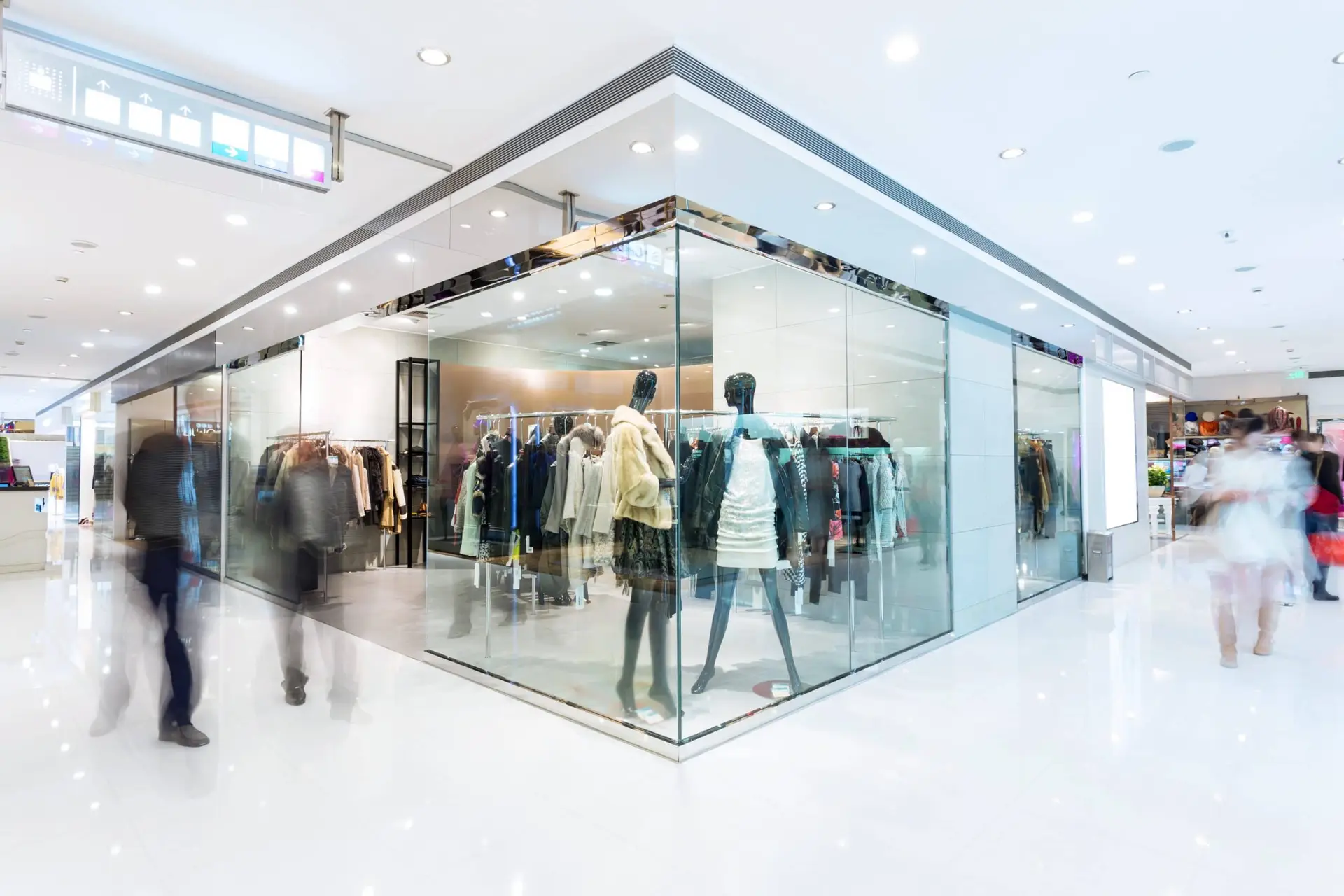 Bright, modern clothing store with glass walls, mannequins in stylish outfits, and shoppers walking by.