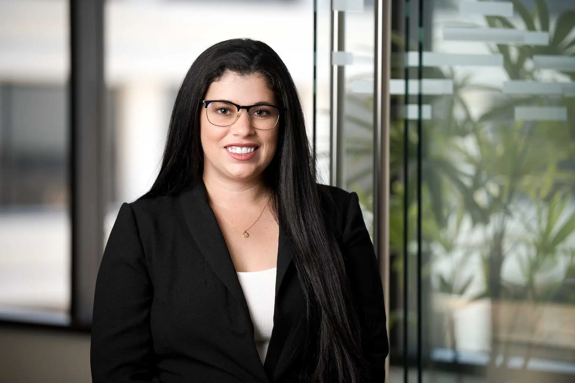 Professional woman in a black blazer wearing glasses, standing in a modern office