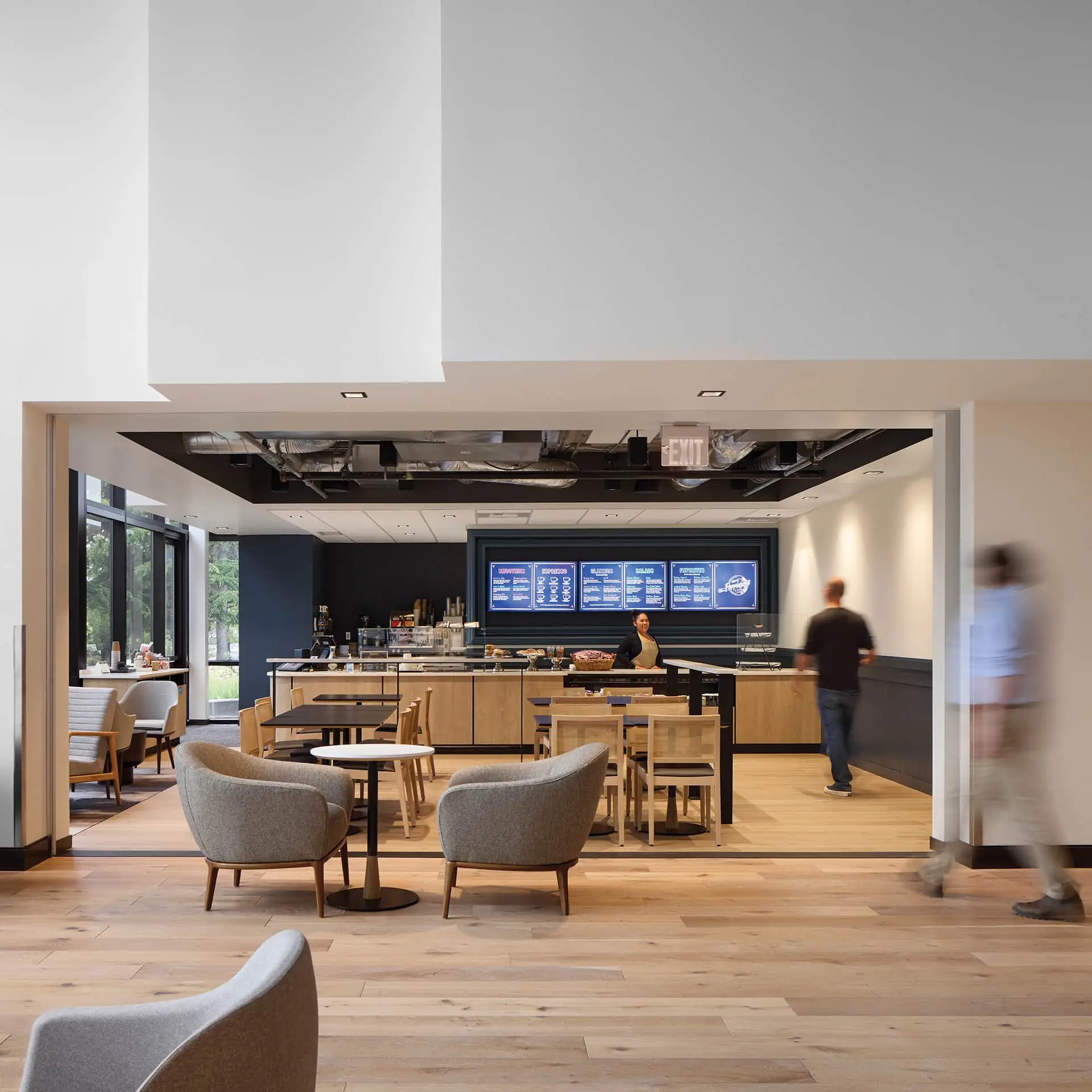 Modern cafe in a bright open lobby with a service counter, menu boards, and light wood seating.
