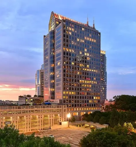 Tall glass skyscraper overlooking a plaza, bathed in sunset light.