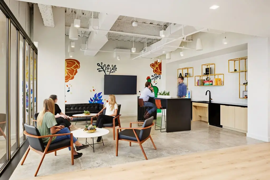 Modern open-plan office lounge with a colorful mural, glass partitions, and a coffee bar.