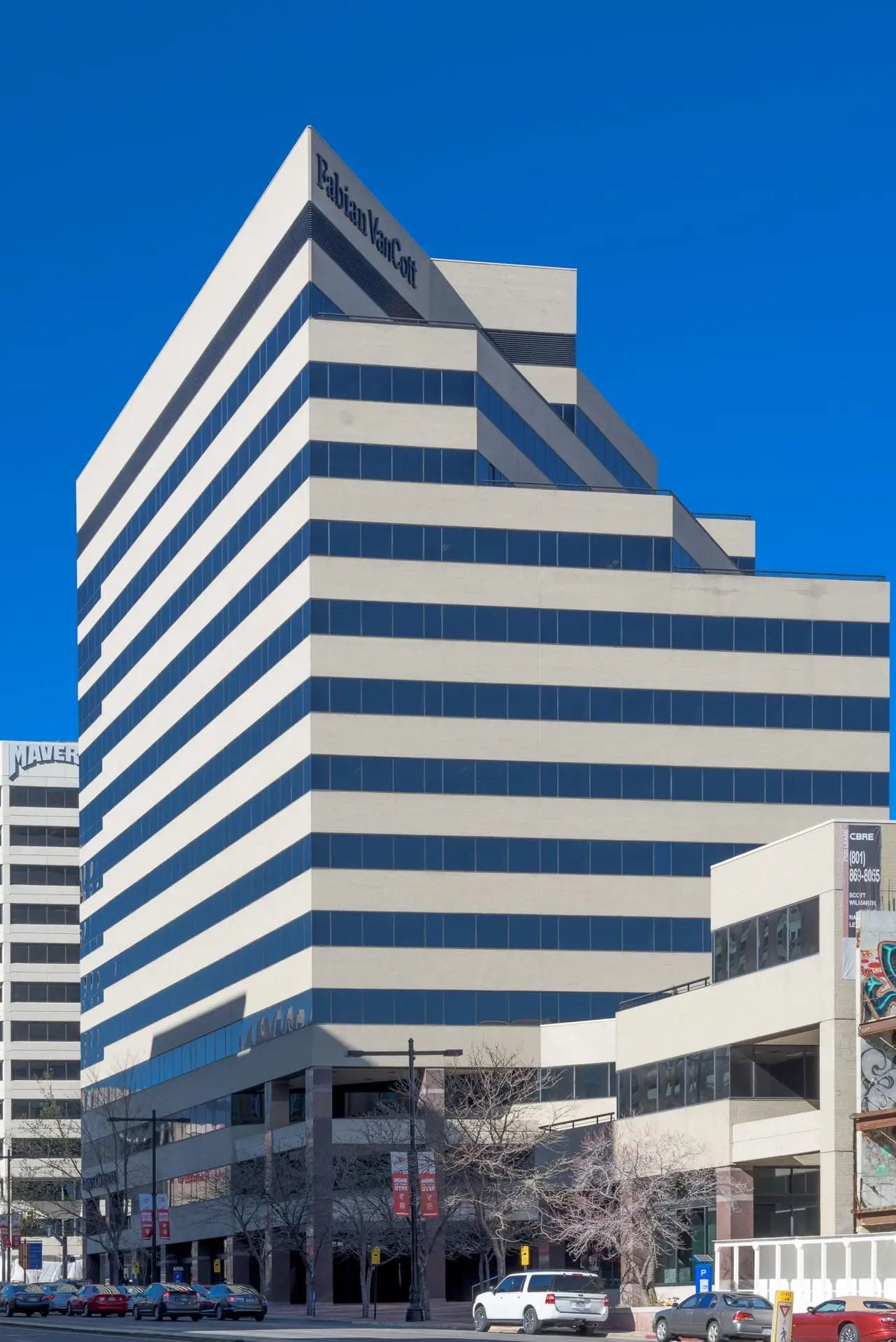 Modern office building with white bands and blue-tinted windows under a clear blue sky.