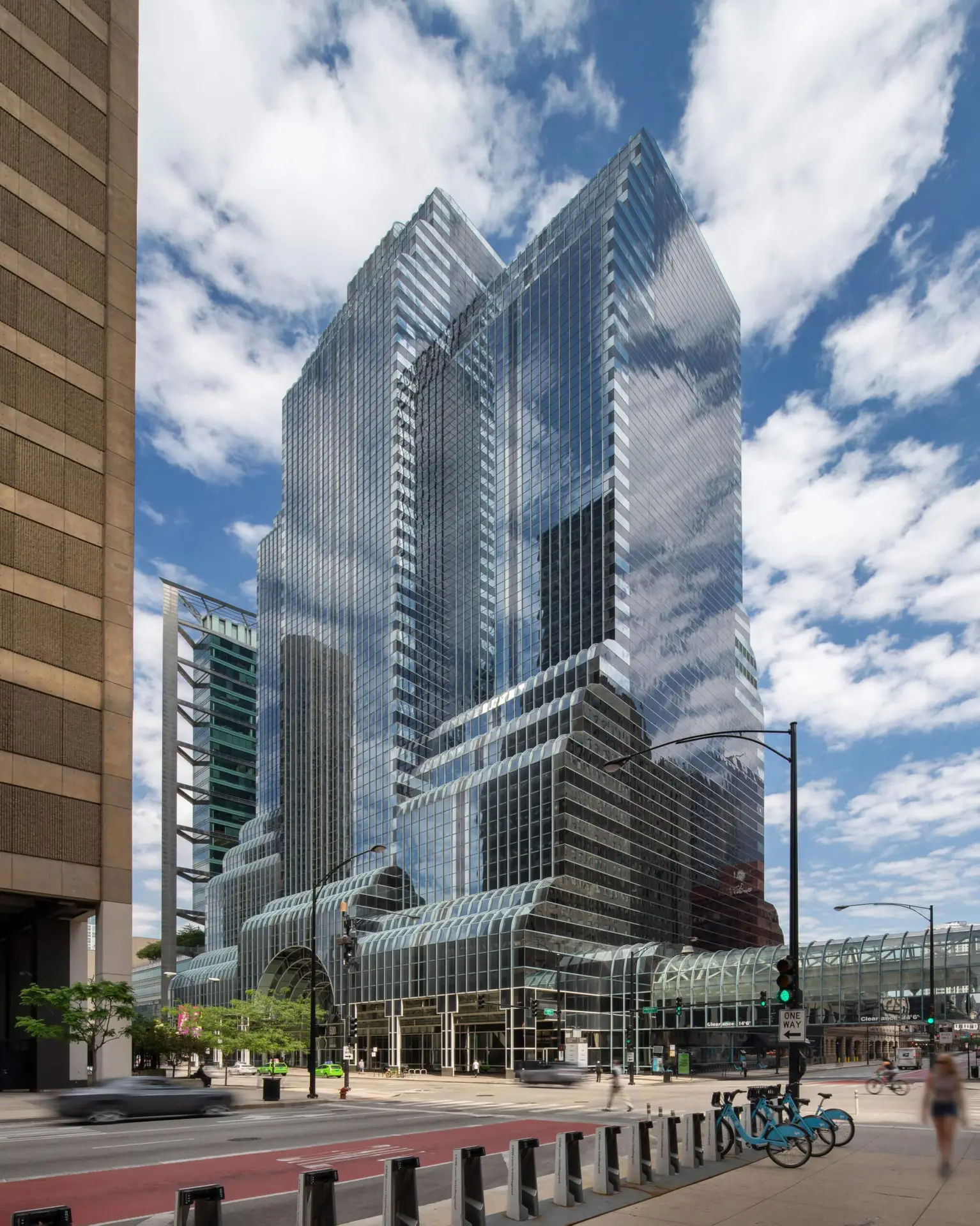 Tall glass skyscraper with reflective facade and curved lower atrium against a blue sky.