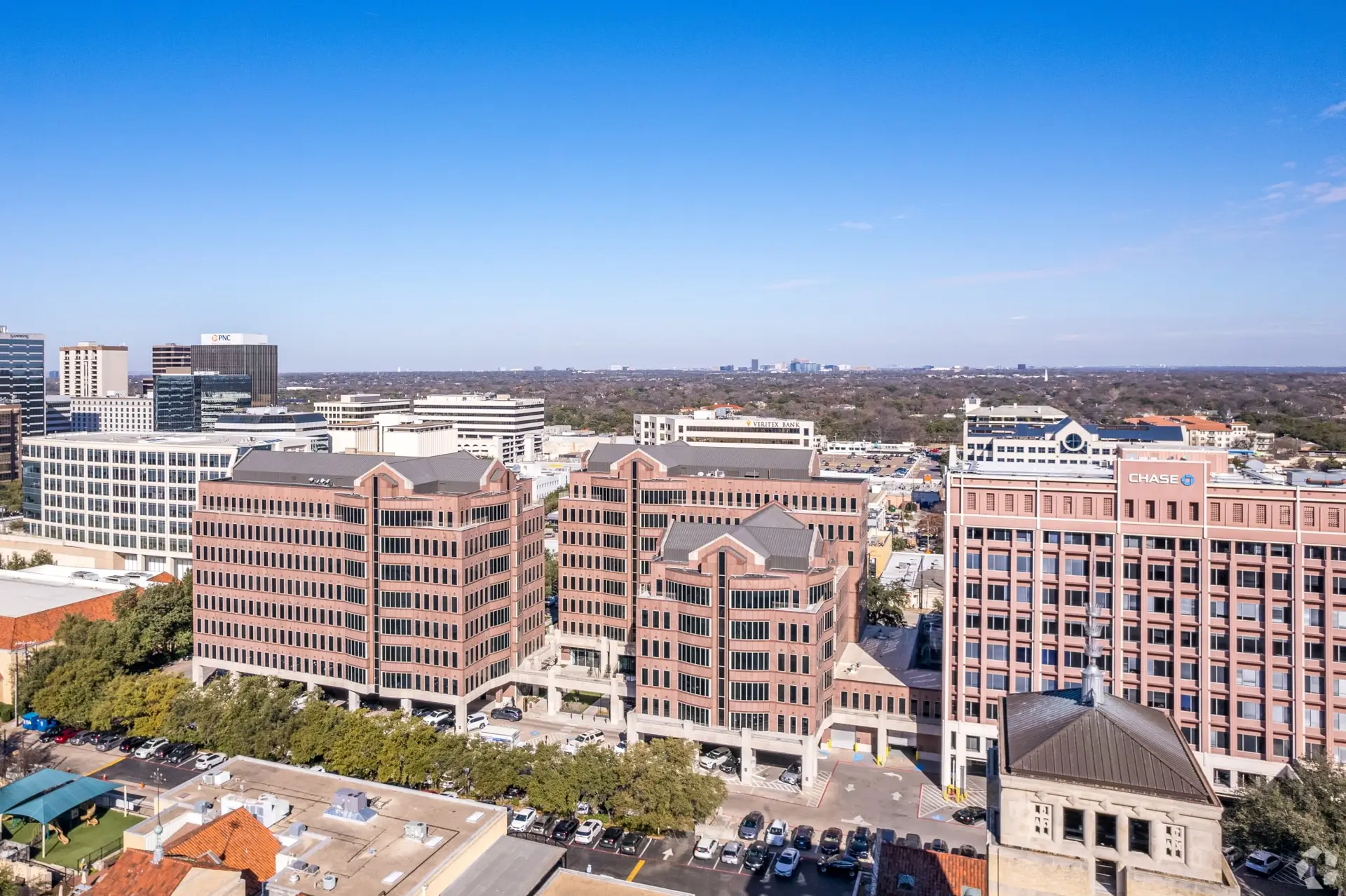 Aerial view of a downtown skyline with red brick office towers, a Chase building on the right, and a clear blue sky.
