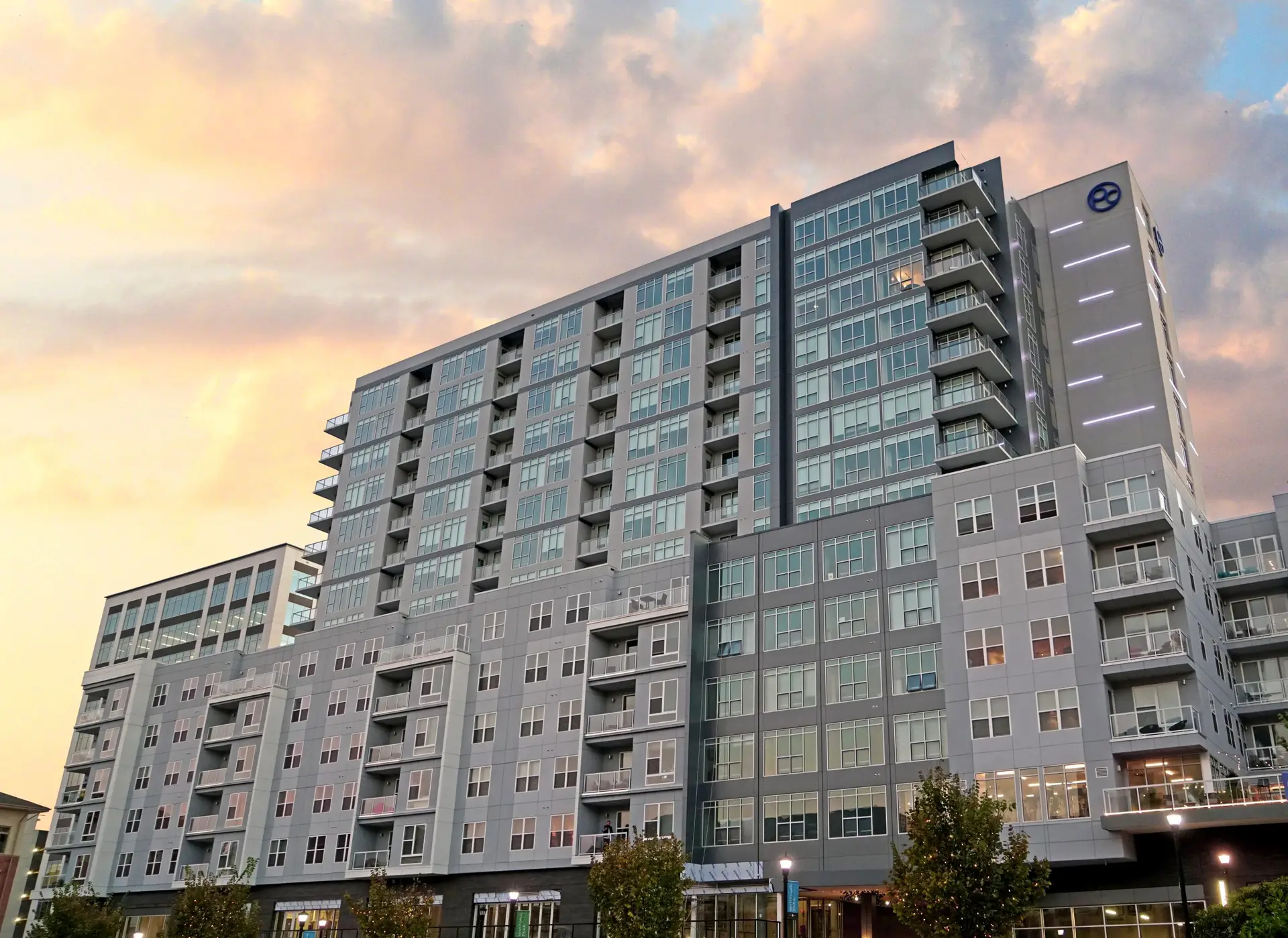Contemporary apartment complex with glass balconies and a tall tower at sunset.