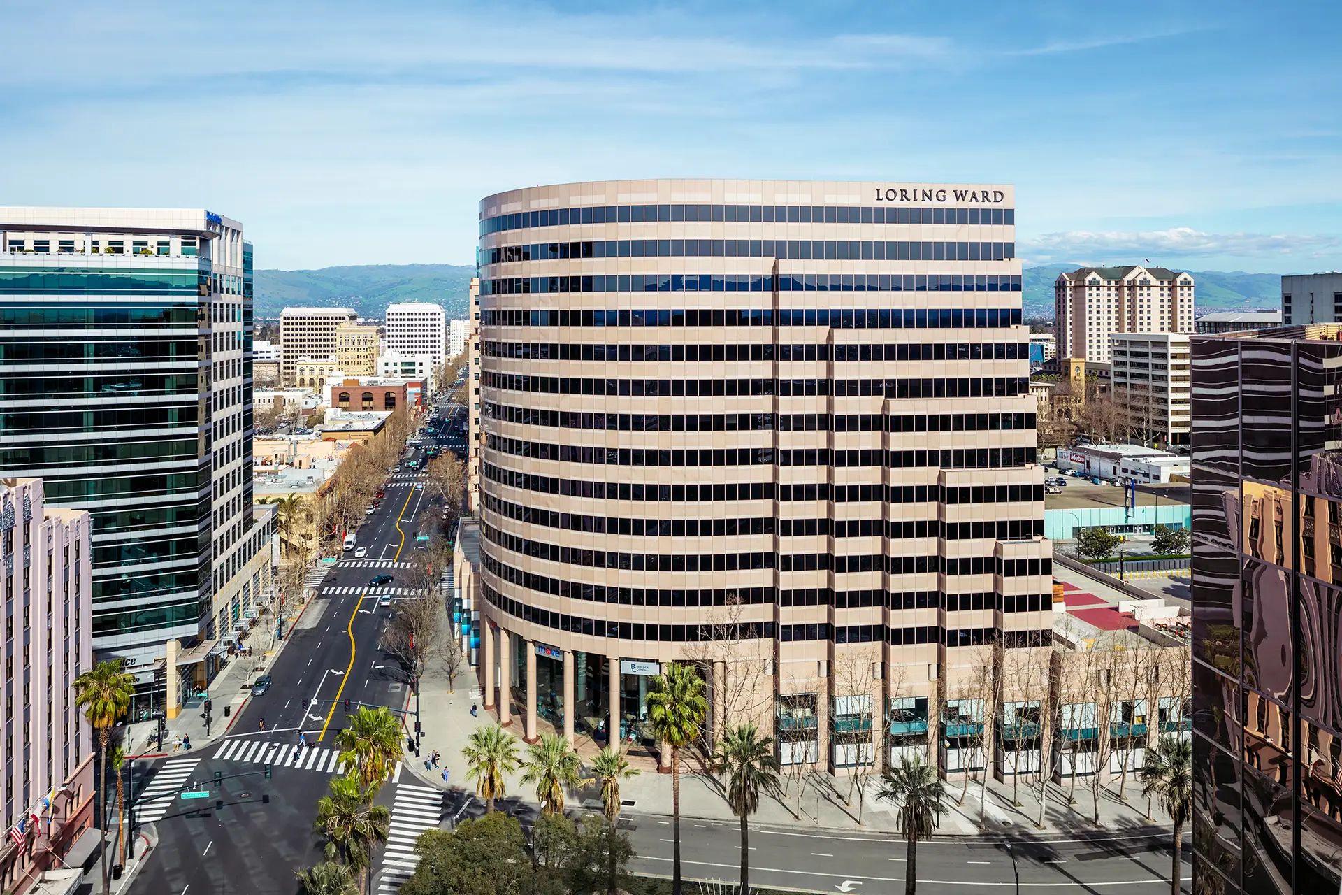 Urban downtown scene with a curved beige office tower labeled Loring Ward, palm trees, and a busy street.