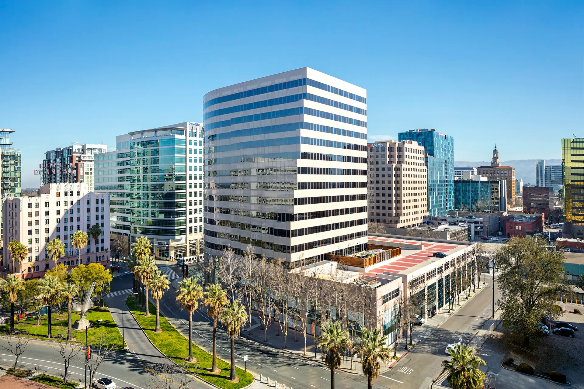 City skyline with modern glass office towers, palm-lined streets, and a clear blue sky.
