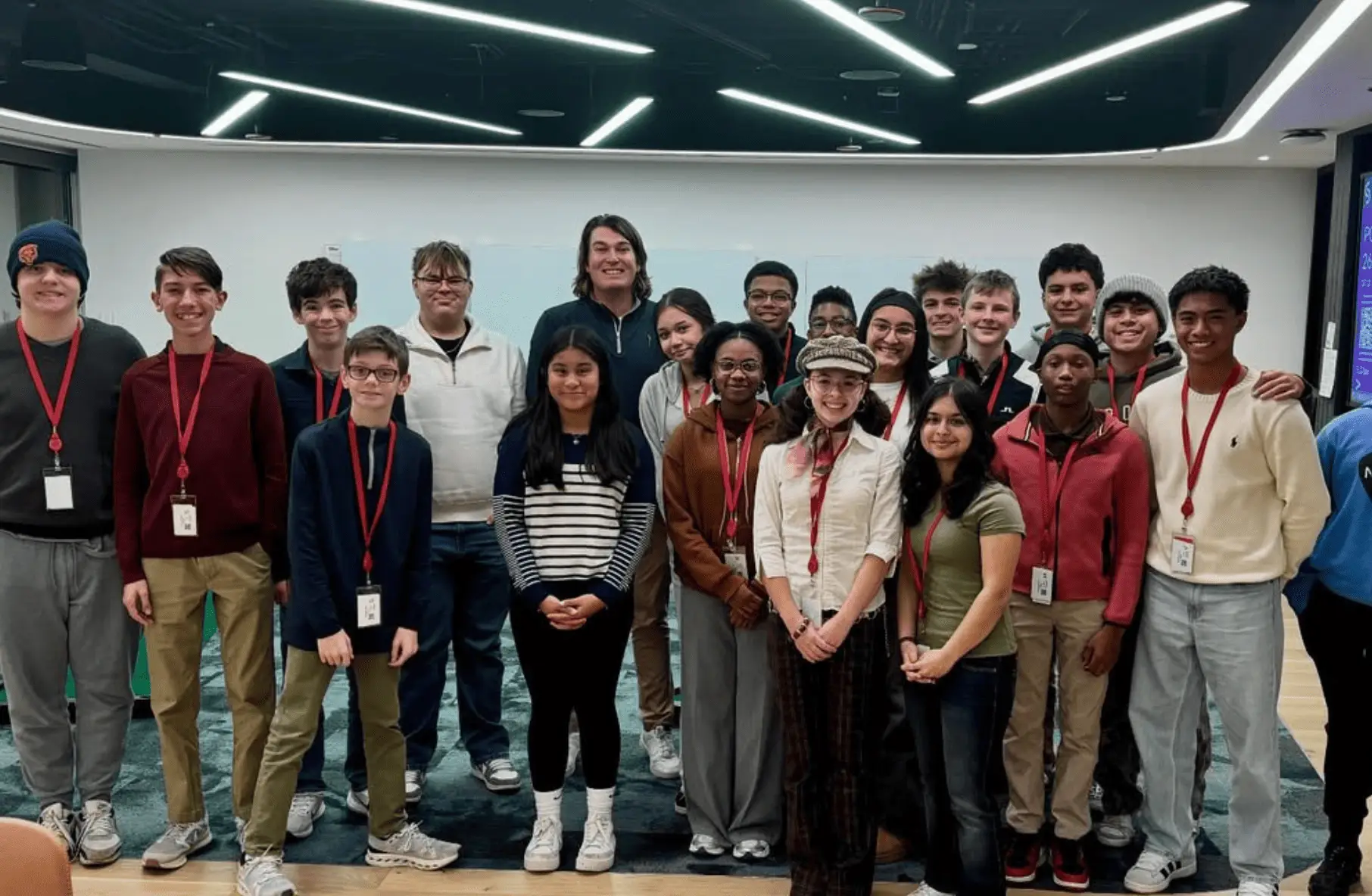Group of diverse students wearing red lanyards posing for a class photo in a modern indoor setting.